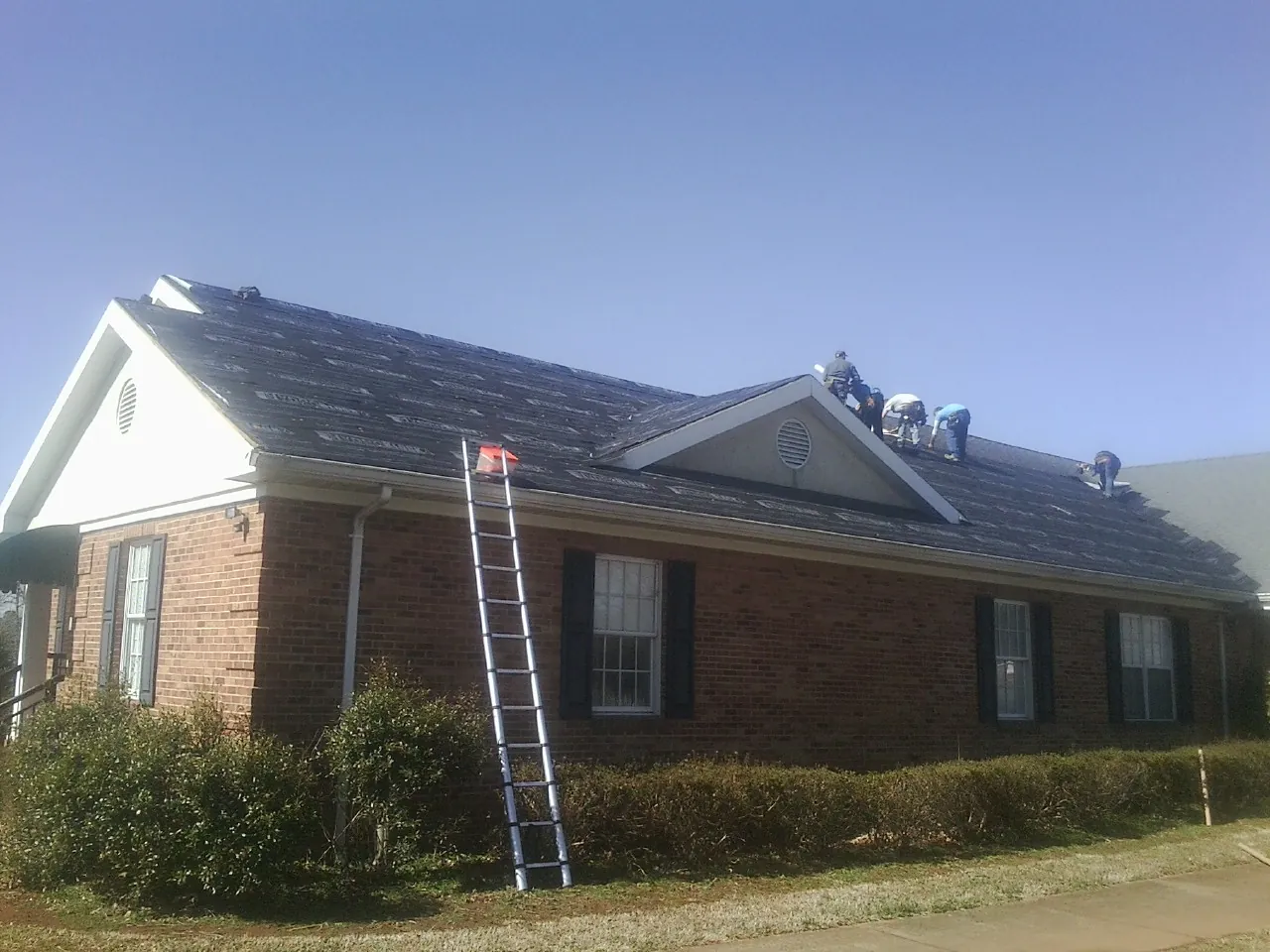Crew tearing shingles off a brick ranch roof with a ladder set — Emergency Roof Repair work by our crew in Harker Heights