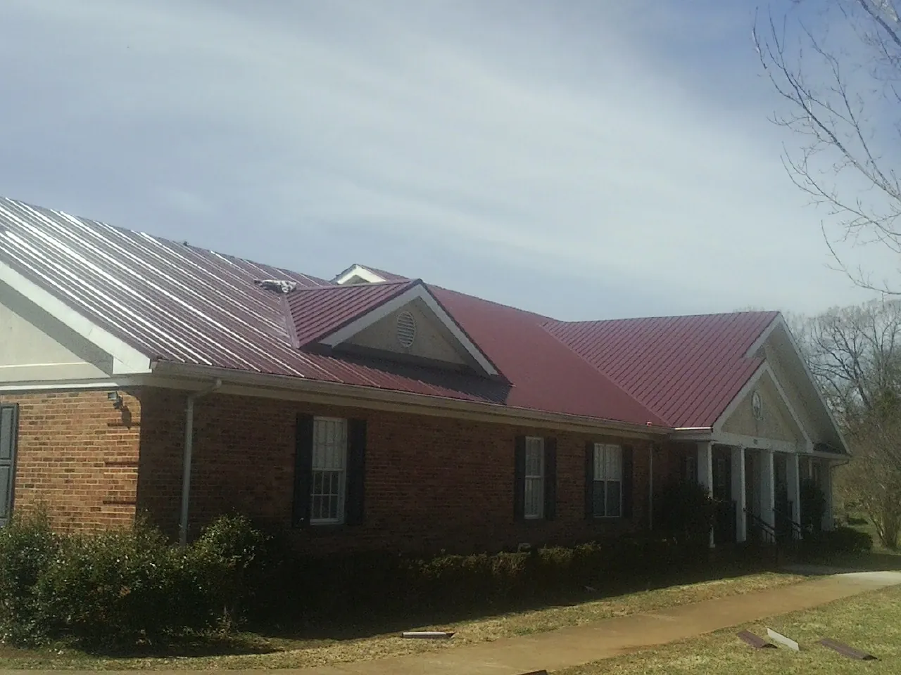 Red metal roof with gabled entries on a long brick building, from a Hail Damage Roof Repair job in Harker Heights