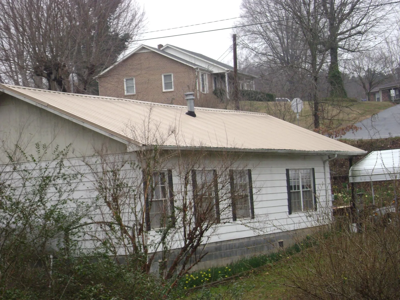 Tan metal roof on a white sided house set into a hillside — Commercial Roofing by Roofing Brothers in Harker Heights
